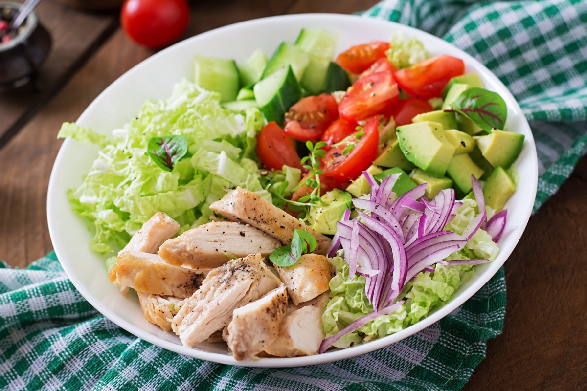A plated salad of grilled chicken, avocado, tomato, cucumber and cabbage